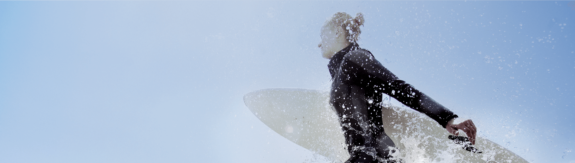 Female surfer running through splashing water with surfboard under arm