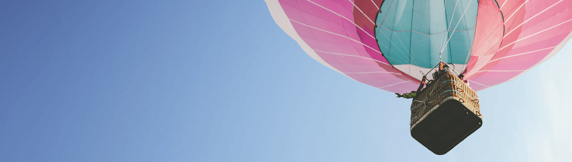 Upward look at a hot air balloon just above the viewer seeing the basket and balloon against a clear blue sky.