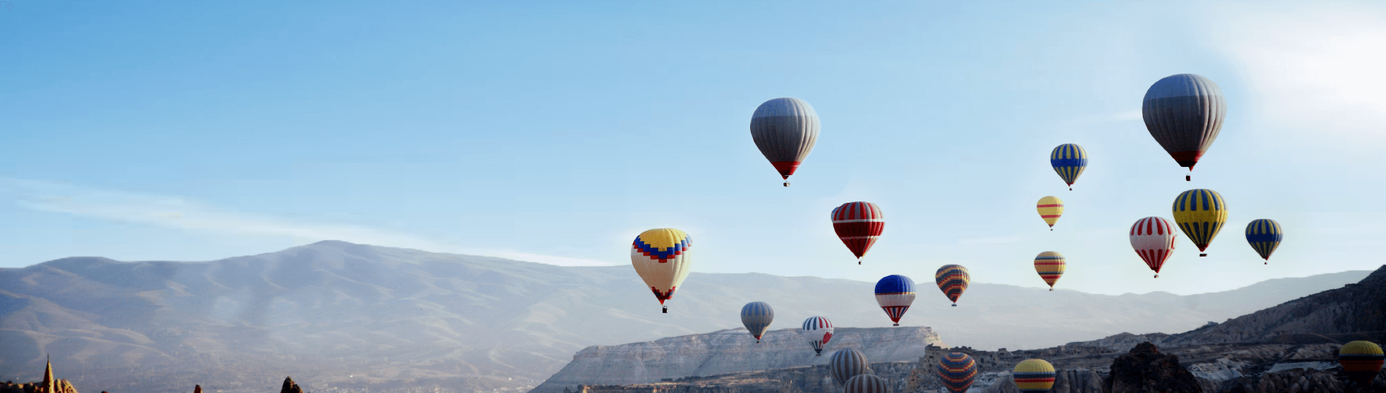 Many hot air balloons over a mountain range.