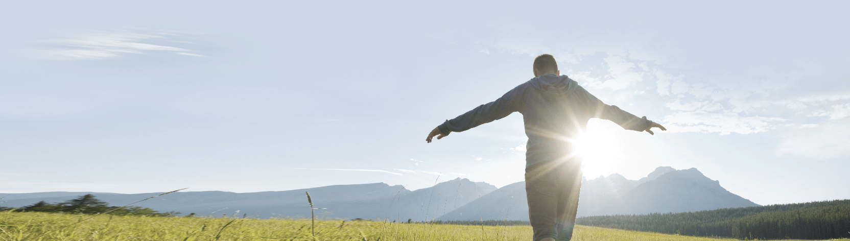 Boy with arms stretched out standing in a field with a mountains backdrop.