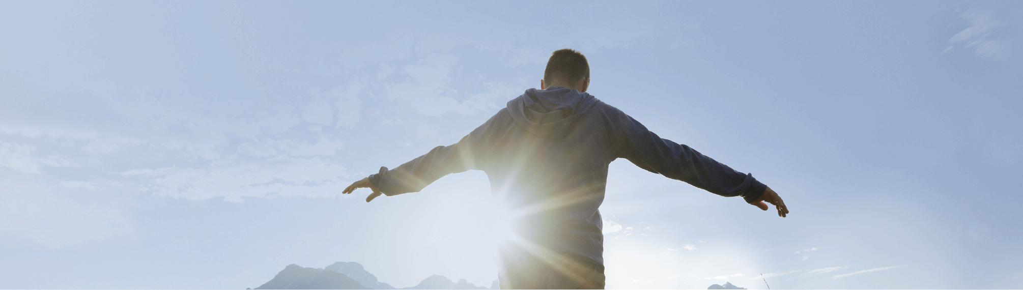 Boy looking at mountain tops standing with arms wide enjoying sun