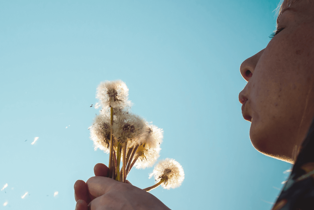 girl blowing dandelion into blue sky